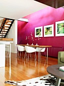 Freundlicher Essbereich mit violetter Wand, langem Esstisch mit Metallfüssen und weissen Designerstühlen