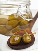 A jar of capers pickled in vinegar and some on a wooden spoon