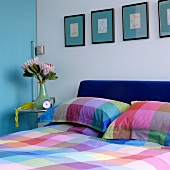 Freundliches Farbspiel im Schlafzimmer mit karierter Bettwäsche unter türkisblauen Passpartouts zu hellblauer Schiebetür