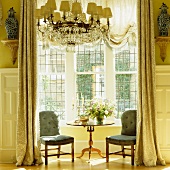 Refined seating area in bay window with floor-length curtains in grandiose interior