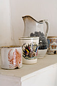 Vintage Becher und Krug aus Porzellan mit traditionellen Motiven auf Ablage
