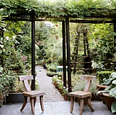 Rustikal moderne Holzstühle auf Terrasse unter berankter Pergola und Blick in blühenden Garten