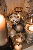 Silberfarbene Weihnachtskugeln neben Kerzenständern mit brennenden Kerzen