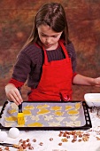A girl brushing biscuits on a baking tray with egg yolk