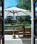 View of seating area on terrace with parasol and garden through open door
