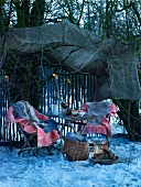 Snowy garden with fire bowl and blankets on garden chairs