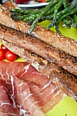 Bread sticks, raw ham, green asparagus and cherry tomatoes
