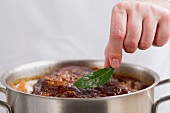 A bay leaf being added braised beef