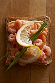 A slice of toast topped with prawns, lemons and chives
