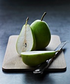 Two pears, whole and halved, on a wooden board with a knife
