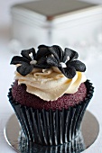 A red velvet cupcake with butter cream and sugar flowers