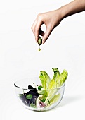 A hand squeezing olive oil from an olive onto a salad