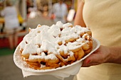 A woman holding a plate of funnel cakes covered in icing sugar at a market