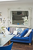 Ornate, Baroque-style wall-mounted mirror above blue sofa in eclectic kitchen-dining room with dark wood flooring