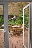 Runde Tischgruppe aus Holz auf begrünter Terrasse mit Backsteinmauer im Hintergrund