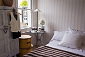 Bedroom with small side table and shabby chic carved wardrobe against striped wallpaper