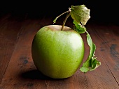A Single Green Apple with Leaf on a Wooden Table