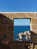 Fensterartige Öffnung in Natursteinmauer mit Blick auf Meeresküste