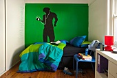 Teenager's bedroom with bed in front of painted figure on green wall
