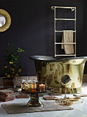 Bad mit orientalischem Flair - brennende Kerzen auf Beistelltisch aus Messing und golden glänzende Badewanne