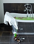 Vintage bathtub with reflective outer surface and slippers on grey tiled floor
