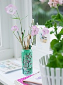 Paintbrushes in can next to potted plant on windowsill