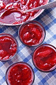 Freshly Made Strawberry Jam in a Pot and Glass Cups on Blue Gingham; From Above