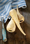 Three parsnips, a tea towel and a peeler on a wooden surface