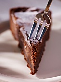 Gabel sticht in ein Stück Schokoladenkuchen mit Puderzucker