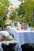 Autumnal table with white table cloth and animal skins on bench in garden