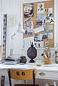 Desk lamp on desk below pinboard on white wooden wall