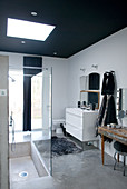 Loft-apartment bathroom with black-painted ceiling above sunken shower base in concrete floor and vintage console table as cosmetics station