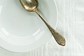 An old silver spoon on a porcelain plate on a linen cloth
