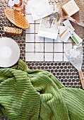 White patterned tiles and scraper next to toiletries and a green hand towel on a mosaic tile floor
