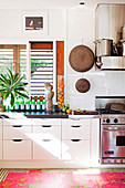 weiße Küche mit Edelstahl-Küchengeräten, Spritzschutz aus Glas und buntem Teppich