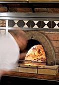 Pizza baker putting pizza into a brick oven