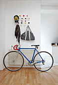 Coat rack made of white wire with colourful spherical hooks above racing bike in open-plan, modern hallway