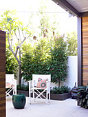 White canvas terrace chair on modern terrace and trees in bordered bed against garden wall