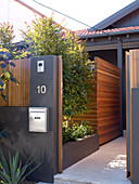 Dark grey garden wall with open gate and view of wooden screen in front of house