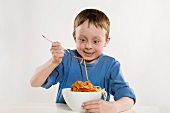 A little boy eating spaghetti with tomato sauce