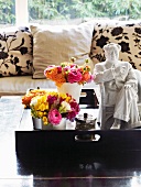 Bouquets in vases next to white china ornament on tray and coffee table in front of sofa with floral cushions