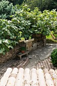 Blick über Vordach auf Steinbank an Natursteinmauer in mediterranem Garten