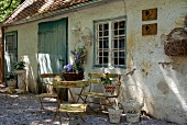 Gartenmöbel aus Eisen und nostalgische Blumenkörbe vor verwitterer Fassade