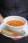 A person holding a bowl of tomato soup garnished with mint