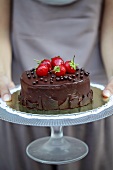 A woman holding a chocolate cake topped with strawberries