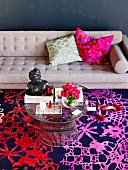 Sitting area in the living room with a gray sofa, carpet in shades of red and purple and a round glass table