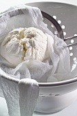 Cream cheese in a muslin cloth and a sieve