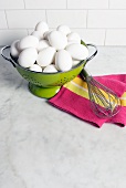 Organic White Eggs in a Green Colander on a Kitchen Counter; Whisk