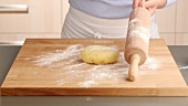 A ball of dough being rolled out on a work surface dusted with flour