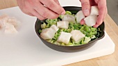 Diced fish being added to a spinach and leek medley